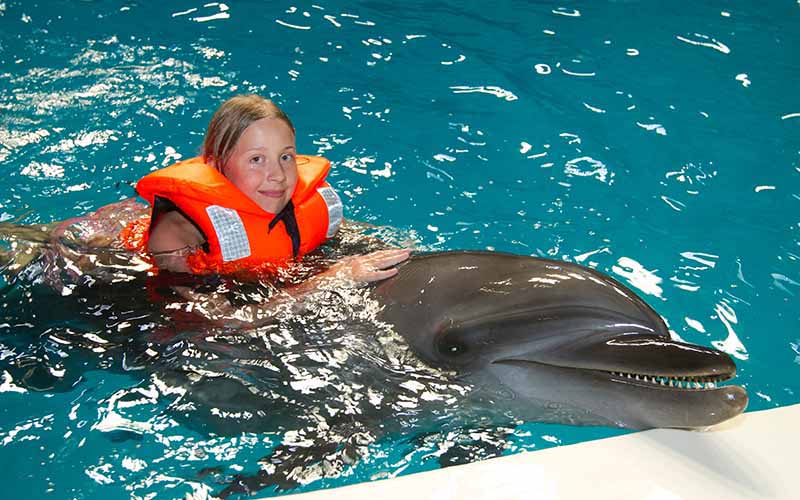 Girl in an orange jacket interacting with a dolphin at Dubai Dolphinarium, a top attraction for marine life shows and experiences.